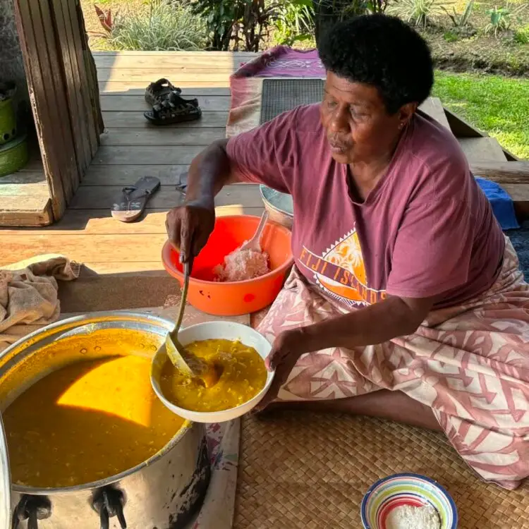 One of the village mothers serve out the large bowls of curry dhal and corned beef with noodles.